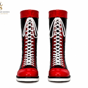 Könnte beinhalten: Ein Paar kniehohe Stiefel mit glänzend schwarzem Schaft, leuchtend roter Zehenkappe und passendem rotem Umschlag am oberen Rand. Die Stiefel werden mit langen weißen Schnürsenkeln durch silberne Ösen gebunden. Das Logo SEVEN STAR SHOES ist sichtbar.
