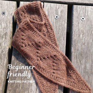Könnte beinhalten: Ein brauner Strickschal mit einem zarten Spitzenmuster und Lochdetails im gesamten Gewebe. Der Schal hat ein spitz zulaufendes Ende und ist mit dem Text "Beginner friendly KNITTING PATTERN" über dem Bild versehen.