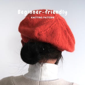 Pode incluir: Uma boina de malha laranja brilhante com uma superfície texturizada e uma banda canelada. O texto "Beginner-friendly KNITTING PATTERN" está impresso em letras brancas acima da boina. O chapéu é usado sobre o cabelo escuro num coque baixo.