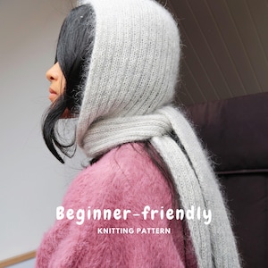 Puede incluir: Una capucha de punto gris claro con bufanda integrada que presenta una textura difusa y un patrón acanalado. La imagen incluye el texto blanco "Beginner-friendly KNITTING PATTERN" superpuesto en el centro de la prenda.