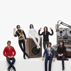 May include: Six Michael Jackson action figures in various outfits including a red cardigan, black military-style jacket, white suit, black zip-up hoodie, blue embellished jacket, and black leather-style outfit, arranged with a vintage reel-to-reel tape recorder.