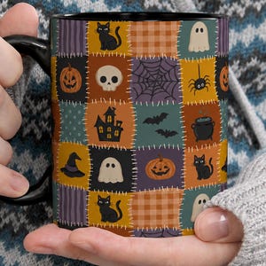 May include: A black ceramic mug featuring a colorful patchwork pattern of Halloween icons including black cats, ghosts, pumpkins, skulls, spider webs, bats, cauldrons, and witch hats, all separated by white stitched lines on a grid background.