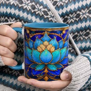 May include: A ceramic mug with a light blue handle and interior, featuring a vibrant stained glass style graphic of a blooming lotus flower in shades of deep blue, turquoise, and gold, set against a dark blue background with intricate patterns.