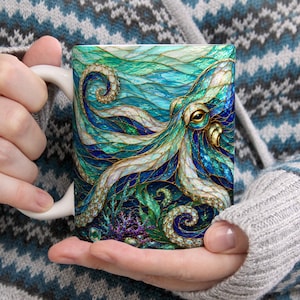 May include: A white ceramic mug featuring a vibrant, stained-glass style illustration of an octopus with swirling tentacles in shades of teal, deep blue, and gold. The design includes intricate patterns and textures, with coral elements at the base.