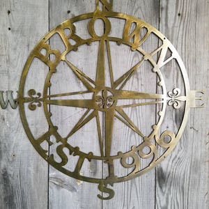 May include: A gold metal compass with the words "Brownville Est 1996" around the edge. The compass has a star in the center and fleur-de-lis designs on the points.