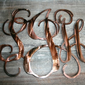 May include: A copper-colored metal monogram with the letters SGH in a cursive script font.