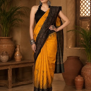 May include: A woman wearing a yellow sari with a black border and accents. The sari is draped over a black halter top. The sari has a patterned design and is accessorized with silver jewelry.