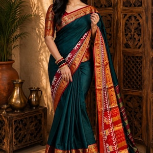 Könnte beinhalten: Ein teal-farbener Sari mit rotem und goldenem Rand. Der Sari weist komplizierte Muster und Designs auf, darunter Elefantenmotive. Die Ärmel der Bluse sind passend rot und gold. Der Sari ist elegant drapiert.