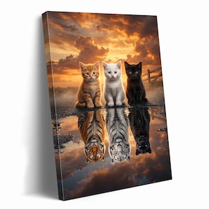 May include: A canvas print featuring three kittens: ginger, white, and black, sitting side-by-side. Their reflections in a puddle below show a tiger, a white tiger, and a black panther. The background is a sunset with orange and yellow hues.