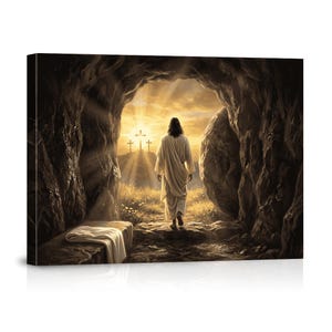 May include: A rectangular canvas print depicting a figure in a long white robe walking out of a dark stone cave toward a bright sunrise. Three crosses are visible on a distant hill. A white cloth is folded on a stone ledge inside the cave entrance.