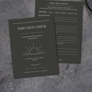 Puede incluir: Dos diarios Daily Self-Check de color gris oscuro. La portada del primer diario tiene el título, un gráfico de sol y texto. El segundo diario está abierto, con indicaciones para el estado de ánimo y los sentimientos. Colección Minimal Wellness.