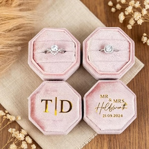 Pode incluir: Quatro caixas octogonais para anéis em veludo rosa seco. Duas caixas contêm anéis prateados com pedras claras. Uma tampa apresenta o texto dourado T | D, a outra o texto dourado MR & MRS Holdsworth 21.09.2024. Dispostas em quadrado.