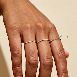 May include: Three thin gold-toned beaded rings worn on the index, middle, and ring fingers. Each ring features a delicate, continuous band of small, uniform metallic spheres. The text Isasoul Etsy is visible in green on the right side of the image.