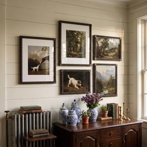Può includere: Una parete galleria con cinque dipinti di paesaggi e animali incorniciati con cornici scure borchiate, disposti sopra una credenza in legno. La credenza ospita vasi in ceramica blu e bianca, piante in vaso, libri e candelabri in ottone.