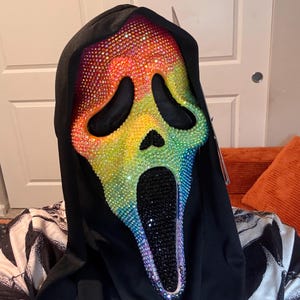May include: A full-head ghost mask featuring a black fabric hood and a face covered in iridescent, rainbow-colored rhinestones. The eye and mouth openings are lined with black material, and the mouth area is filled with solid black rhinestones.