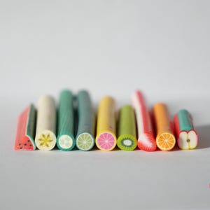 Peut inclure: Une collection de tranches de fruits miniatures, dont pastèque, carambole, citron vert, citron, kiwi, fraise, orange et pomme. Chaque tranche est de couleur vive et détaillée, mettant en valeur les textures et les motifs des fruits.