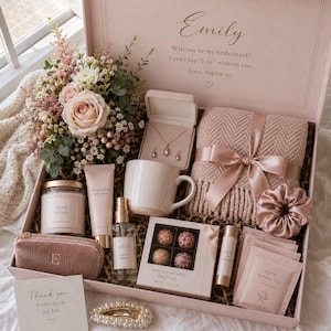Könnte beinhalten: Eine Geschenkbox mit einem Strauß rosa Blumen, einem Schmuckset mit Halskette und Ohrringen, einer rosa Strickdecke mit Schleife, einem Becher, einer Kerze, Handcreme, Rosenspray, Schokoladentrüffeln, Lippenbalsam, Teebeuteln und einem Haargummi.