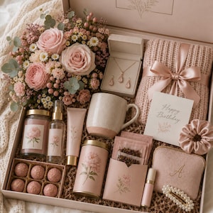 Op de afbeelding: Een geschenkdoos met een boeket roze rozen en madeliefjes, een sieradenset met ketting en oorbellen, een roze gebreide deken met lint, een Happy Birthday-kaart, een mok, een kaars, een sprayfles, een tube, theezakjes en een etui.