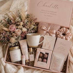 May include: A gift box containing a dried floral arrangement, a ceramic mug, a candle labelled Blush Rose, rosewater hand cream, lip balm, a perfume spray, rose truffles, a rose quartz necklace and earring set, a scrunchie, and rose herbal tea.