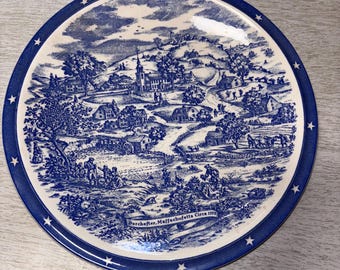 Könnte beinhalten: Ein blau-weißes Zierteller mit einer ländlichen Szene mit einer Kirche, Häusern und Figuren. Der Teller hat einen blauen Rand mit weißen Sternen und dem Text "Dorchester, Massachusetts Circa 1775".