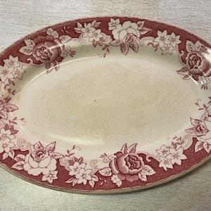 May include: An oval-shaped serving platter with a white background and a red floral design around the edge. The flowers are roses and smaller white flowers.