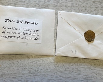 Może przedstawiać: Biała koperta z etykietą z napisem "Black Ink Powder" i instrukcjami dotyczącymi mieszania proszku z wodą. Koperta jest zaklejona złotą pieczęcią woskową.