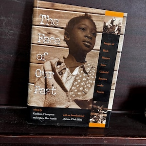 Puede incluir: Portada de libro con el título "The Face of Our Past: Images of Black Women from Colonial America to the Present" editado por Kathleen Thompson e Hilary Mac Austin con una introducción de Darlene Clark Hine. La portada presenta una foto en blanco y negro de una joven negra.