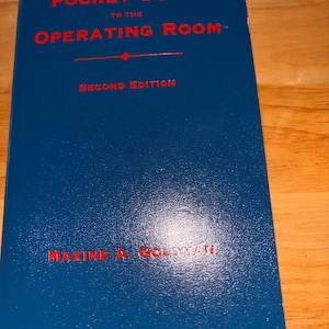 Op de afbeelding: Een blauw boek met de titel "Pocket Guide to the Operating Room" in rode letters. De omslag bevat ook "Second Edition" en de naam van de auteur, Maxine A. Goldman.