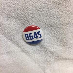 May include: A red, white, and blue button with the number 8645 printed in blue.