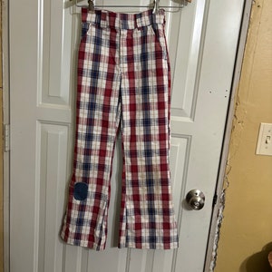 Puede incluir: Pantalón de campana de cuadros rojo, blanco y azul con un parche azul en la rodilla izquierda.