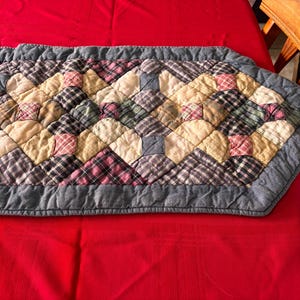 K&ouml;nnte beinhalten: Gesteppter Tischl&auml;ufer mit Rautenmuster. Der L&auml;ufer hat ein Patchwork-Design mit Quadraten aus karierten und unifarbenen Stoffen in Beige-, Rosa-, Gr&uuml;n- und Graut&ouml;nen. Die Kanten sind mit einem grauen Rand versehen.