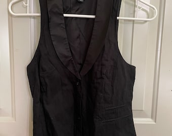 May include: A black sleeveless vest with a satin collar and a single button closure. The vest has two pockets on the front and a label that reads "H&M" on the inside.