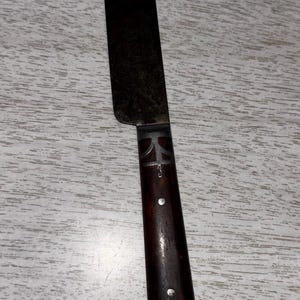 Puede incluir: Un cuchillo de mantequilla vintage plateado con un mango de madera oscura. El mango tiene un diseño decorativo con una cruz en el extremo.