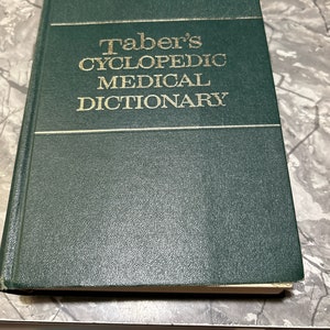 Puede incluir: Un libro de tapa dura verde con el título "Taber's Cyclopedic Medical Dictionary" en letras doradas.
