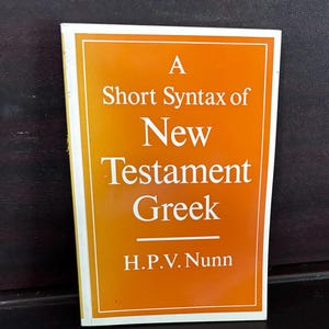 May include: A rectangular book with a vibrant orange cover and a white border. The title A Short Syntax of New Testament Greek is printed in white serif font, followed by the author name H.P.V. Nunn in white text at the bottom of the cover.