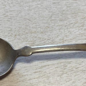 以下が含まれることがあります： 丸みを帯びたボウルと細長い柄が付いた銀のスプーン。柄にはボウルの近くに装飾的な要素があり、刻印されたイニシャルが付いたハート型の端があります。スプーンはおそらくヴィンテージです。