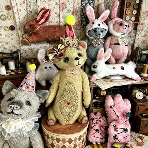 May include: A collection of handmade plush toys, including teddy bears and rabbits, in various colors. The teddy bears wear party hats and crowns, while the rabbits have bunny ears. The toys are displayed on a table with sewing supplies.
