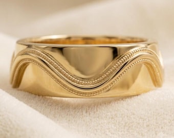 May include: A polished gold band ring featuring a continuous, raised wavy line design that wraps around the circumference. The surface of the wave is detailed with a fine, beaded texture, creating a distinct contrast against the smooth gold finish.