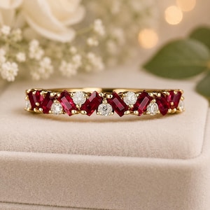 Puede incluir: Un anillo de oro con un patrón alterno de rubíes rojos en talla baguette y diamantes blancos en talla redonda. Las piedras preciosas están engastadas horizontalmente a lo largo de la parte superior del anillo, creando un diseño simétrico.