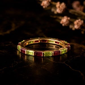 Può includere: Una fede in oro con pietre preziose alternate, granati rossi e peridoti verde chiaro, tagliate a baguette e incastonate in un canale continuo. L'anello presenta un motivo ripetitivo di pietre rettangolari lungo l'intera circonferenza della fascia.