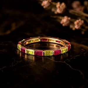 Könnte beinhalten: Ein goldener Eternity-Ring mit abwechselnd im Baguetteschliff geschliffenen roten Rubinen und lindgrünen Peridoten, die in einer durchgehenden Schiene gefasst sind. Der Ring zeigt einen lebendigen Farbkontrast durch die tiefroten und hellgrünen Steine.