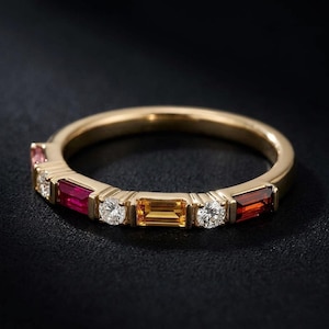 Könnte beinhalten: Ein Goldring mit einem abwechselnden Muster aus im Baguetteschliff geschliffenen Edelsteinen in Rot-, Orange- und Gelbtönen, durchsetzt mit runden, klaren Steinen im Brillantschliff. Die Metallfassung ist aus poliertem Gold gefertigt.