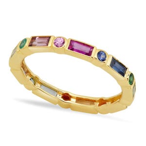 Könnte beinhalten: Ein goldener Bandring mit einem abwechselnden Muster aus mehrfarbigen Edelsteinen. Das Design umfasst rechteckige Baguette-Schliff-Steine in Pink, Blau und Grün, durchsetzt mit kleinen runden Schliff-Steinen in pinken, blauen und grünen Farbtönen.