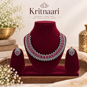 Pode incluir: Um conjunto de colar e brincos prateados com pedras retangulares rosa-escuras. As joias estão expostas num busto de veludo vermelho-escuro. O texto Kritnaari e Timeless Jewellery For Your Unique Story é visível na parte superior.