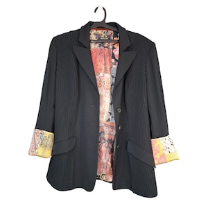 Pode incluir: Um blazer preto com detalhes plissados verticais nos painéis frontais, lapela entalhada e três botões. O forro interior e os punhos dobrados das mangas exibem uma estampa multicolorida com motivos florais e animais variados.