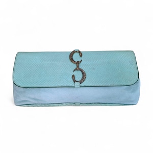 Puede incluir: Un bolso de mano rectangular con una solapa turquesa texturizada con un patrón similar a la piel de serpiente y una base azul claro lisa. El centro de la solapa está asegurado por un cierre metálico en tono bronce con forma de dos serpientes entrelazadas.