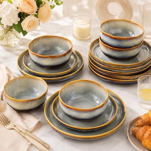 May include: A set of ceramic dinnerware featuring bowls and plates with a reactive glaze finish. The pieces display a gradient colour scheme transitioning from a deep blue base to a light grey centre, finished with a warm brown rim on each edge.