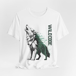 Puede incluir: Camiseta blanca con un diseño de lobo geométrico en negro, blanco y verde. El lobo aúlla, con un efecto de cuadrícula digital en su cuerpo. El texto "WILDCODE" está impreso verticalmente en verde en el lado derecho.