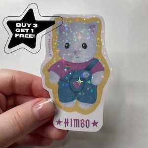 May include: A holographic sticker featuring a grey cat character wearing a pink shirt and blue overalls. The sticker has a gold border, a small rainbow heart on the shirt, and the text HIMBO at the bottom. A black star-shaped graphic says BUY 3 GET 1 FREE.