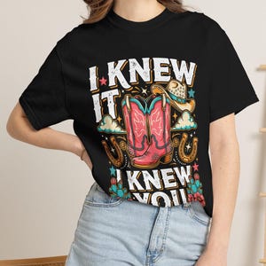 Pode incluir: Uma t-shirt preta com uma estampa gr&aacute;fica de botas de cowboy cor-de-rosa, um chap&eacute;u de cowboy bege, ferraduras e cactos. O texto "I KNEW IT" e "I KNEW YOU" est&aacute; impresso em letras brancas desgastadas em torno da ilustra&ccedil;&atilde;o central.